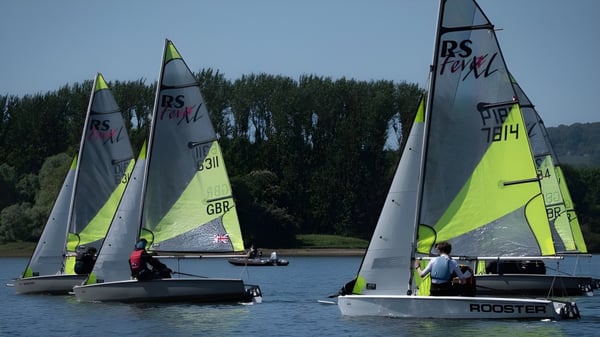 Segelboote gleiten über ein ruhiges Gewässer vor einer grünen Landschaft auf dem Campus des Cardiff Sixth Form College.