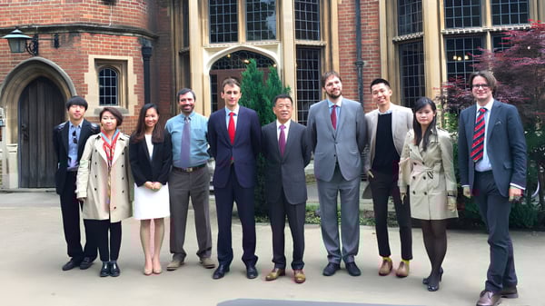 Eine Gruppe von Personen in formeller Kleidung steht vor einem Backsteingebäude mit Rundbogenfenstern auf dem Gelände des Carfax College.