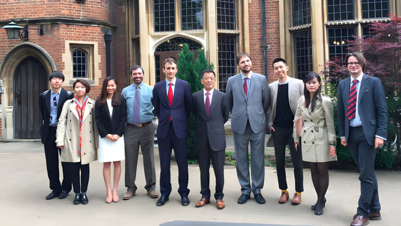 Eine Gruppe von Personen in formeller Kleidung steht vor einem Backsteingebäude mit Rundbogenfenstern auf dem Gelände des Carfax College.