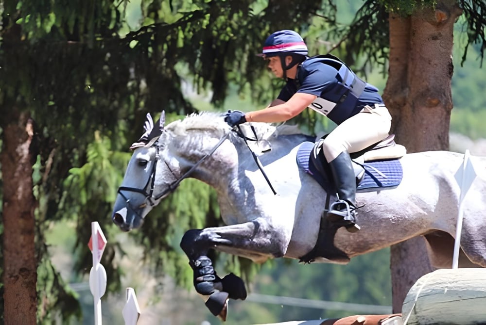 Eine Schülerin von Carfax College sitzt auf einem weißen Pferd in einer bewaldeten Umgebung.