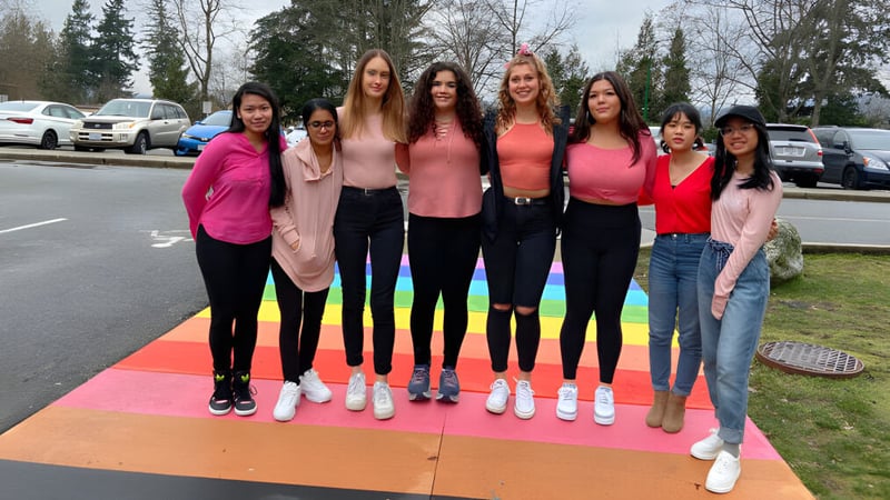 Eine Gruppe Schülerinnen der Cariboo Hill School steht auf einer bunten Außenterrasse vor Bäumen und geparkten Fahrzeugen.