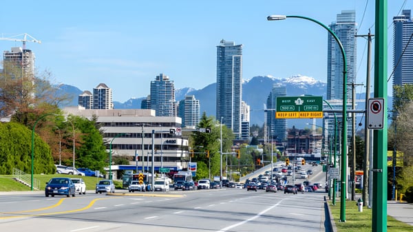 Blick auf eine belebte Straße mit Hochhäusern und Bergen im Hintergrund nahe der Cariboo Hill School.