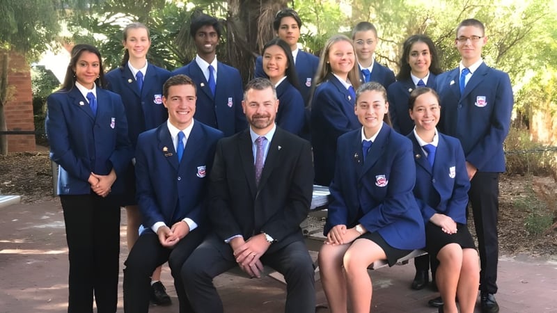 Eine Gruppe Schüler der Carine Senior High School steht im Freien vor einem Backsteingebäude mit Bäumen im Hintergrund.