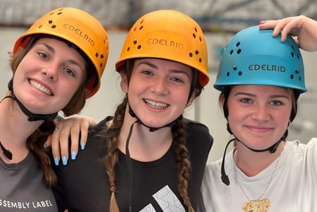 Drei Schülerinnen der Carine Senior High School tragen gelbe und blaue Helme und posieren gemeinsam in einem Innenraum.