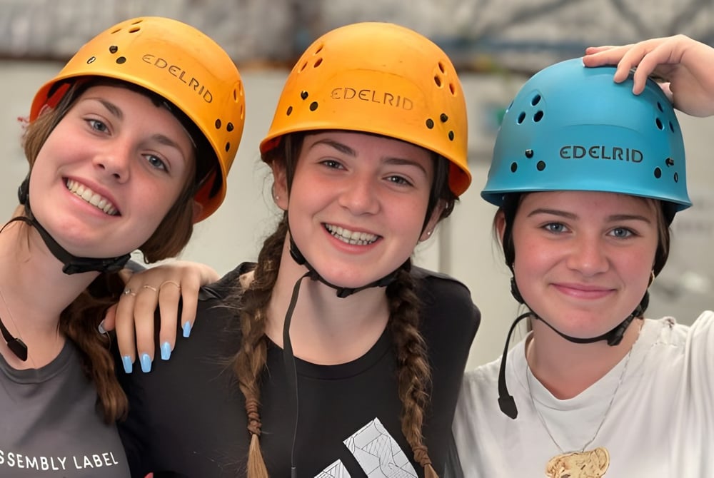 Drei Schülerinnen der Carine Senior High School tragen gelbe und blaue Helme und posieren gemeinsam in einem Innenraum.