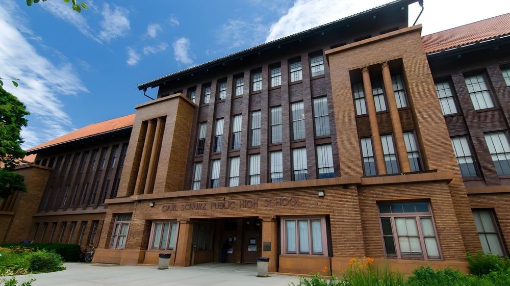 Das mehrstöckige Backsteingebäude der Carl Schurz High School steht in einem gepflegten Außenbereich mit grünen Pflanzen.