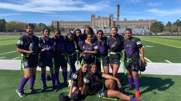 Eine Gruppe Schüler in Sportuniformen posiert auf dem Sportfeld vor dem historischen Gebäude der Carl Schurz High School.
