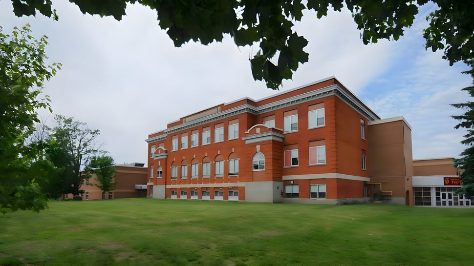 Das große Backsteingebäude von Carleton Place High School steht auf einem Rasenfeld umgeben von grünen Bäumen.