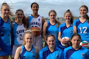Eine Gruppe junger weiblicher Basketballspielerinnen posiert im blauen Trikot auf einem Sportplatz des Carmel College.