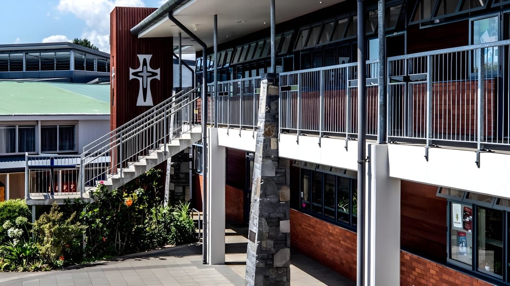 Das moderne mehrstöckige Gebäude mit kreuzförmigem Design auf dem Campus des Carmel College ist von Grünanlagen und einem gepflasterten Weg umgeben.