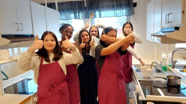 Eine Gruppe junger Frauen mit roten Schuerzen steht in der Kueche des Carmelitas Cadiz Colegio und macht Handgesten.