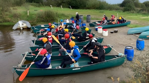 Schüler der Carrigallen Vocational School sitzen in bunten Schwimmwesten auf Kanus auf einem Fluss mit dichter Vegetation.