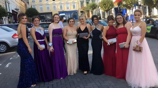 Eine Gruppe junger Frauen in festlicher Kleidung steht auf der Straße vor dem Carrignafoy Community College.