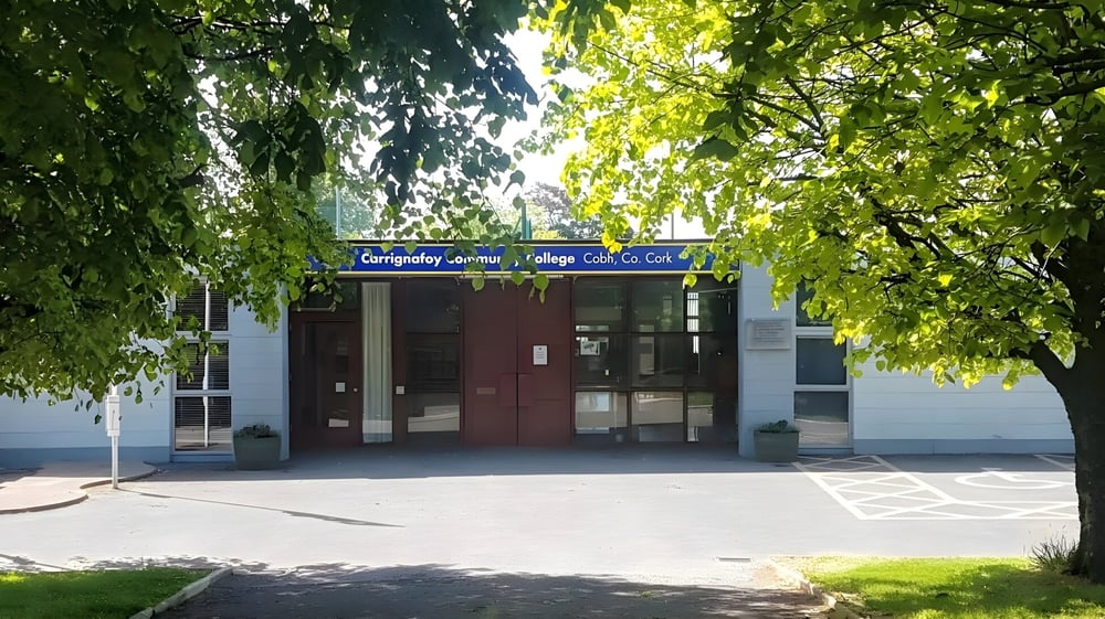 Der Eingang des Carrignafoy Community College mit einem Backsteingebäude und grünen Bäumen im Hintergrund.