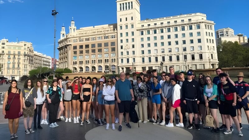 Eine Gruppe von Schülerinnen und Schülern steht vor dem historischen Gebäude des Carrignafoy Community College in der Stadt.