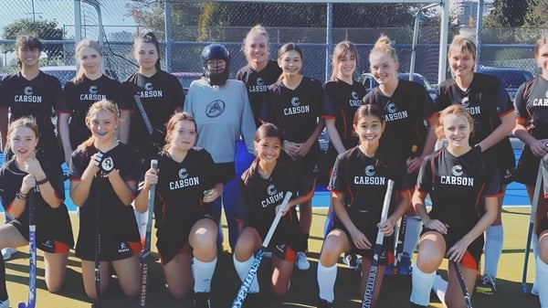 Eine Gruppe junger Athletinnen posiert gemeinsam auf dem Sportfeld der Carson Graham Secondary School.