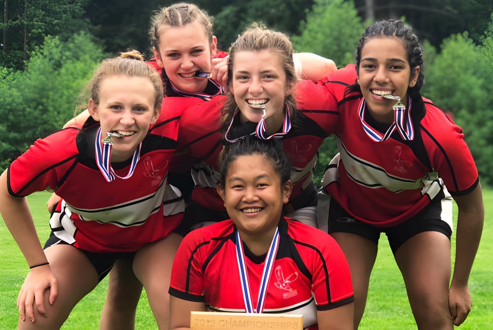 Eine Gruppe junger Frauen in roten Uniformen mit Medaillen steht auf einer Wiese auf dem Gelände der Carson Graham Secondary School.