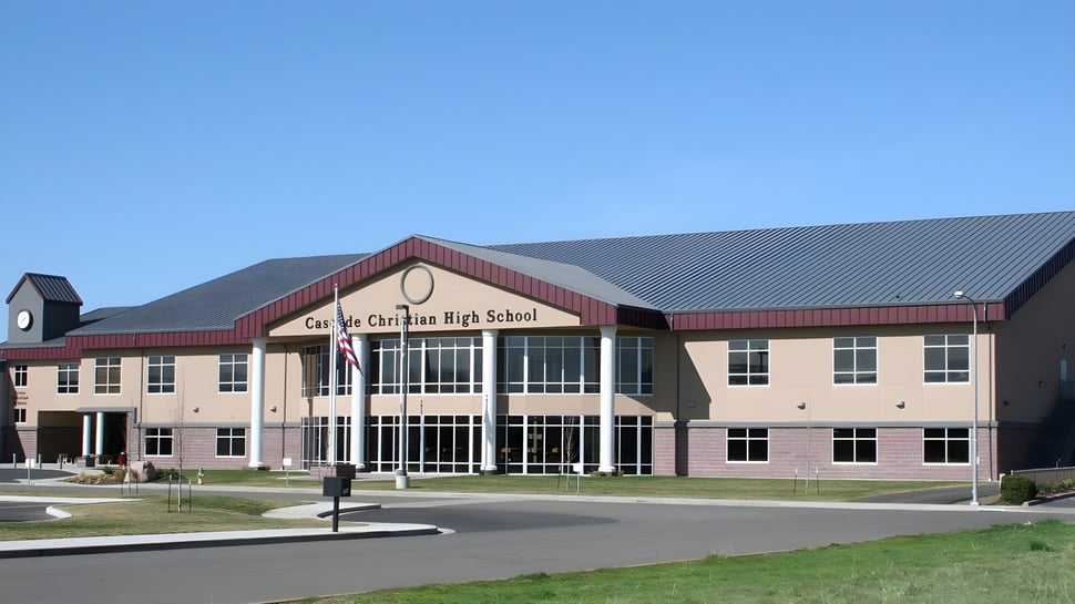Das moderne Schulgebäude der Cascade Christian High School mit rotem Ziegeldach und Glasfront bei klarem Himmel.