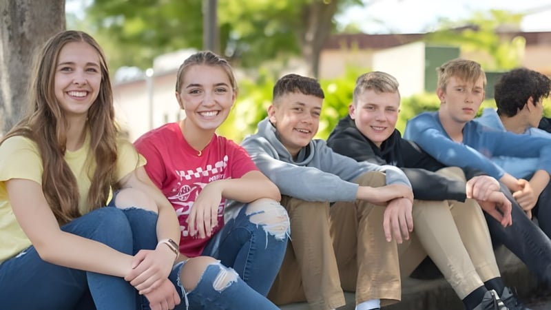 Eine Gruppe von Schülerinnen und Schülern der Cascade Christian High School sitzt im Freien vor Bäumen und Grünfläche zusammen.