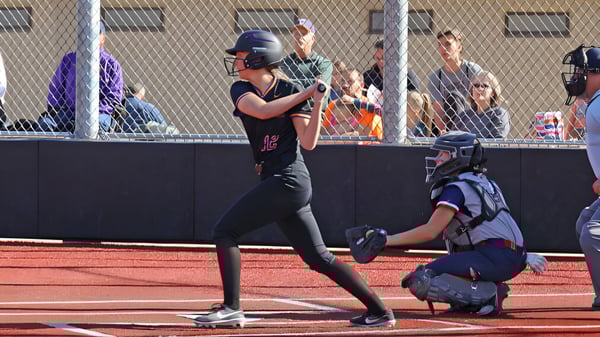 Ein Softball-Spieler in schwarzer Uniform steht auf dem Spielfeld der Cascade Christian High School mit einem Fänger in blauer Uniform hinter der Heim Basis.