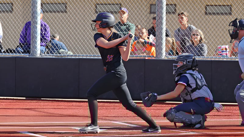 Ein Softball-Spieler in schwarzer Uniform steht auf dem Spielfeld der Cascade Christian High School mit einem Fänger in blauer Uniform hinter der Heim Basis.