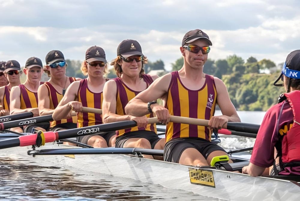 Schüler der Cashmere High School beim Rudern auf einem Gewässer mit einer Landschaft im Hintergrund.