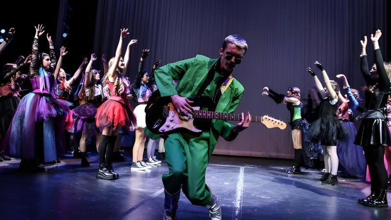 Ein Musiker in grüner Kleidung spielt auf der Bühne vor einer Tanzgruppe auf dem Campus der Castlepollard Community College.