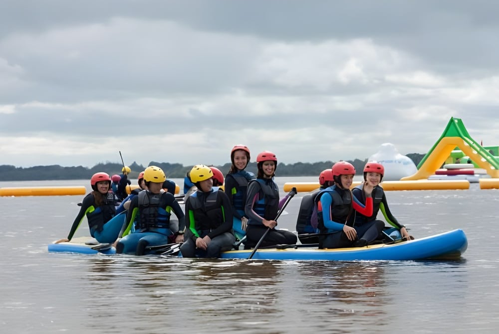 Schüler der Castlerea Community School paddeln gemeinsam in bunten Schwimmwesten auf einem Schlauchboot während einer Outdoor-Aktivität.