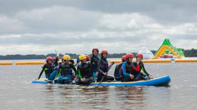 Schüler der Castlerea Community School paddeln in bunten Schwimmwesten auf einem großen Schlauchboot bei einem Outdoor-Rafting auf dem Wasser.