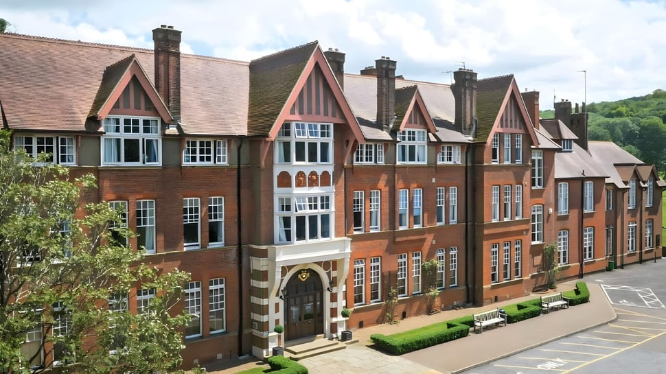 Das mehrstöckige Backsteingebäude der Caterham School im Tudorstil ist von üppigem Grün umgeben.