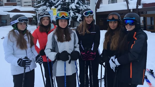 Eine Gruppe junger Schülerinnen der Caterham School trägt Wintersportkleidung und steht in einer verschneiten Außenanlage mit Gebäuden im Hintergrund.