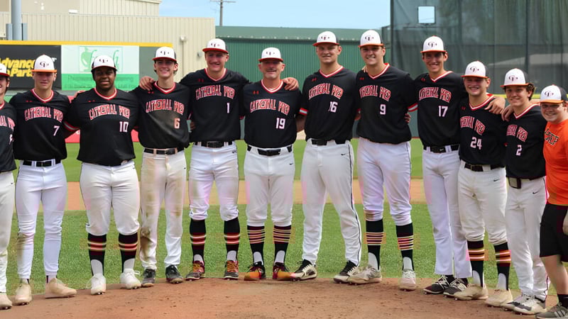 Schüler der Cathedral Preparatory School stehen in Baseballuniform mit Helmen auf dem Baseballfeld vor einem Gebäude.