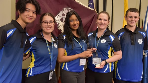 Eine Gruppe Schülerinnen und Schüler der Cathedral School of St Anne & St James steht zusammen vor einem roten und weißen Hintergrund bei einer Veranstaltung.