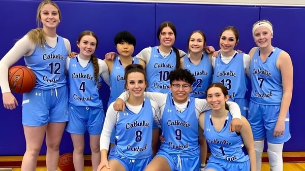 Eine Gruppe von Schülerinnen in blauen Basketballuniformen posiert vor einer blauen Wand auf dem Campus der Catholic Central High School.