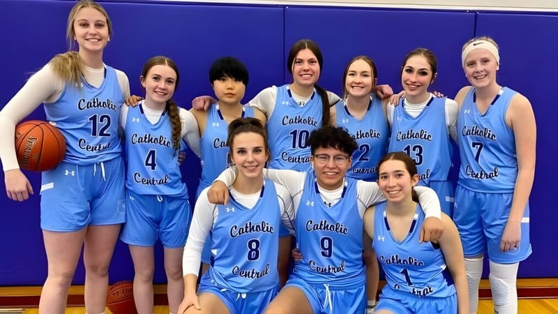 Eine Gruppe von Schülerinnen in blauen Basketballuniformen posiert vor einer blauen Wand auf dem Campus der Catholic Central High School.