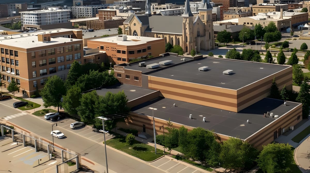 Das Hauptgebäude der Catholic Central High School ist von Bäumen umgeben und Teil einer Stadtsilhouette mit modernen und historischen Gebäuden.