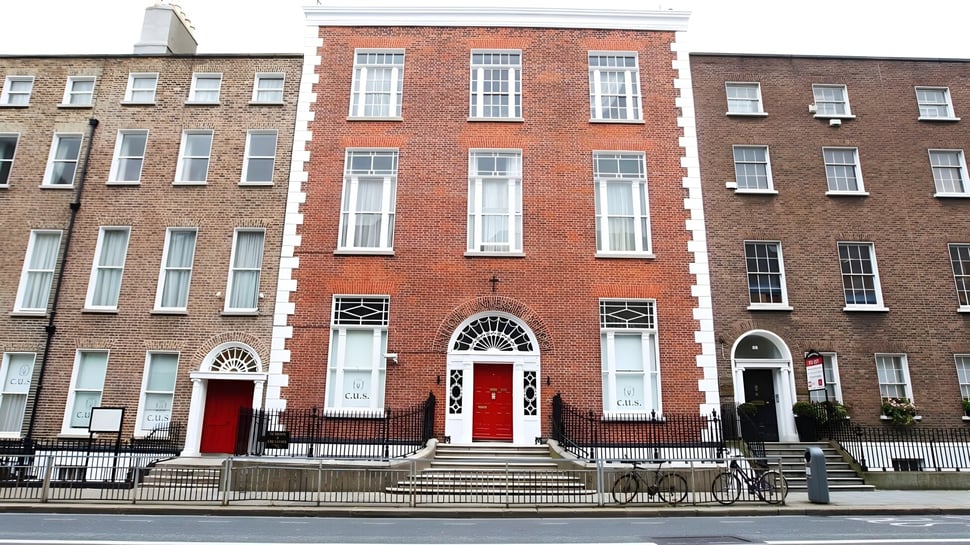 Das mehrstöckige Backsteingebäude mit Rundbogenfenstern und roten Türen gehört zur Catholic University School.