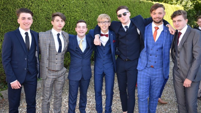 Eine Gruppe formell gekleideter Personen posiert gemeinsam vor grünem Hintergrund auf dem Campus der Catholic University School.