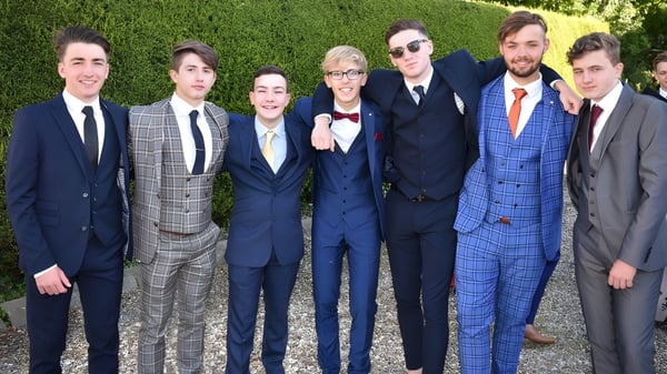 Eine Gruppe gut gekleideter Personen posiert vor einer grünen Hecke auf dem Gelände der Catholic University School.