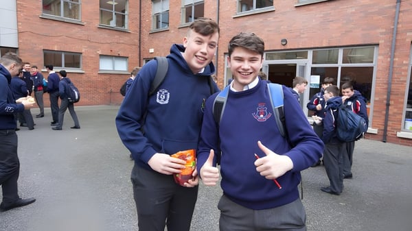 Zwei Schüler in Schuluniform stehen gemeinsam und lächeln vor einem Backsteingebäude auf dem Campus der Catholic University School.