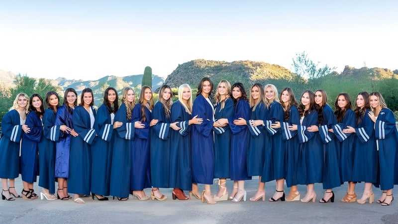 Studentinnen des Cave Creek Unified School District posieren in blauen Abschlussroben vor einer Berglandschaft.