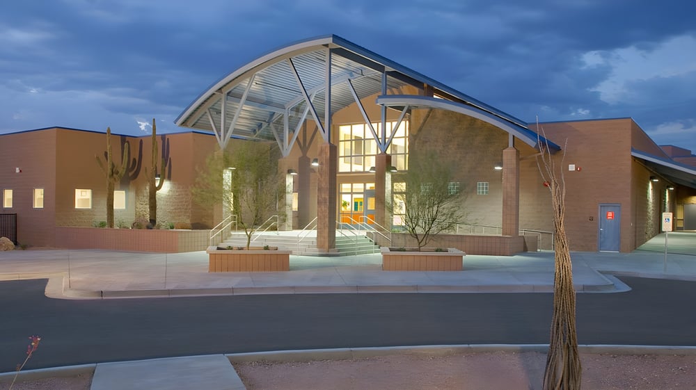 Das moderne Gebäude mit Glasfront und geschwungenem Dach auf dem Gelände des Cave Creek Unified School District ist von Bäumen umgeben.