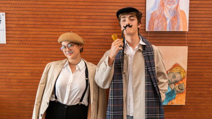 Zwei Personen stehen vor einer orangefarbenen Wand mit Kunstwerken auf dem Campus des Caxton College.