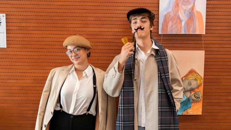 Zwei Personen stehen vor einer orangefarbenen Wand mit verschiedenen Kunstwerken auf dem Campus des Caxton College.