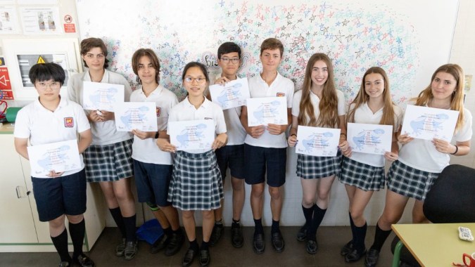 Schüler des Caxton College stehen gemeinsam im Klassenzimmer und zeigen ihre Arbeiten.