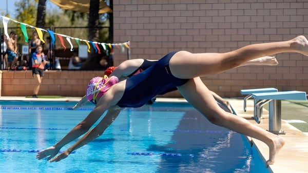 Eine Schülerin oder ein Schüler des Caxton College taucht im Schulschwimmbad ins Wasser, im Hintergrund sind bunte Fahnen zu sehen.