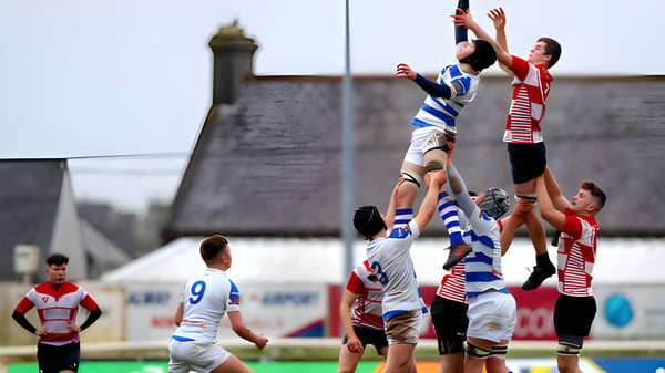 Zwei Rugbyspieler kämpfen um den Ball in der Luft vor einem historischen Gebäude auf dem Campus der C.B.S. Roscommon.