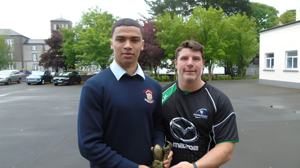 Zwei Schüler der C.B.S. Roscommon stehen im Freien mit Bäumen und Gebäuden im Hintergrund.