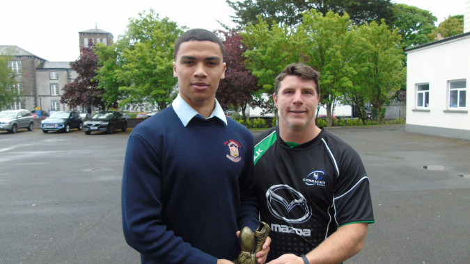 Zwei Schüler der C.B.S. Roscommon stehen zusammen im Außenbereich mit Bäumen und Gebäuden im Hintergrund.