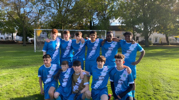 Eine Gruppe junger Fußballspieler in blauen Trikots auf einem grünen Spielfeld auf dem Campus der CBS Westland Row.